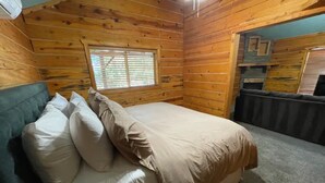 Una camera in una baita di legno con un letto, cuscini, una finestra e un piccolo angolo cottura.