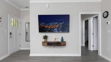 A hallway with a mounted TV displaying a nighttime cityscape, a wooden console table with decorative items, and a clock on the wall.