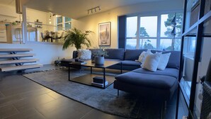 Un salon moderne avec un canapé aux couleurs sombres, une table basse et une grande fenêtre offrant une vue sur l’extérieur.
