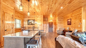 L’intérieur d’une cabane en bois comprend un coin cuisine, un espace repas et un salon avec un canapé et des fauteuils.