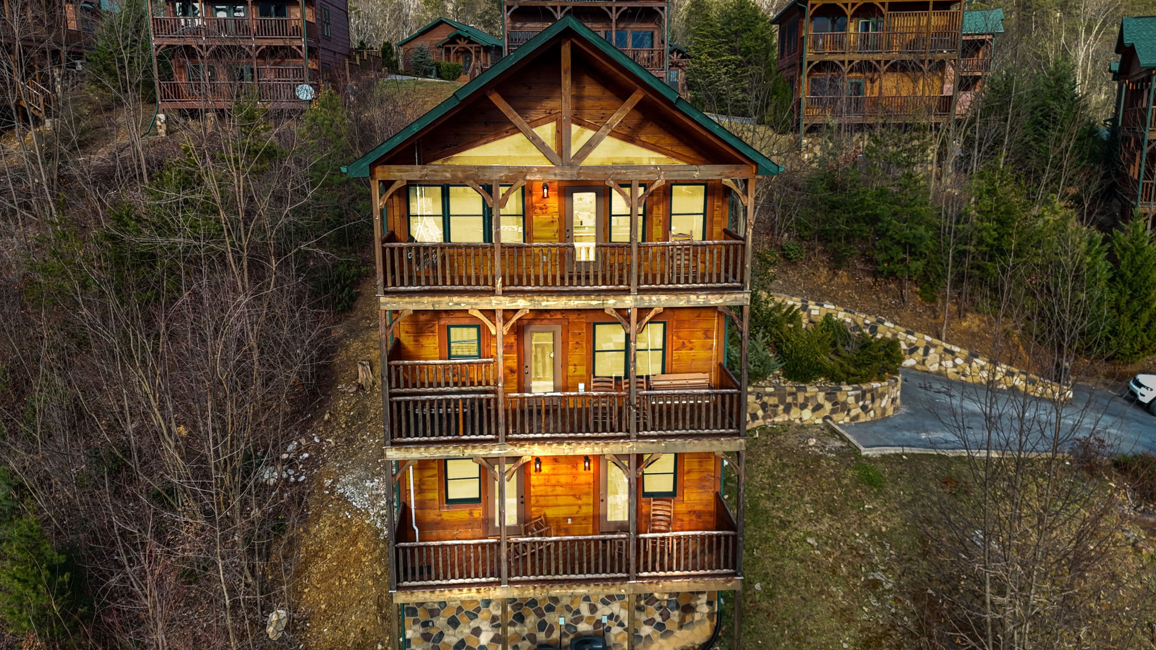 A multi-story log cabin with a balcony on the second floor, surrounded by trees and a stone pathway.