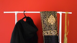 Un mur rouge sur lequel est fixée une étagère blanche, où sont posés un manteau noir, un vêtement à motifs et un chapeau rouge.
