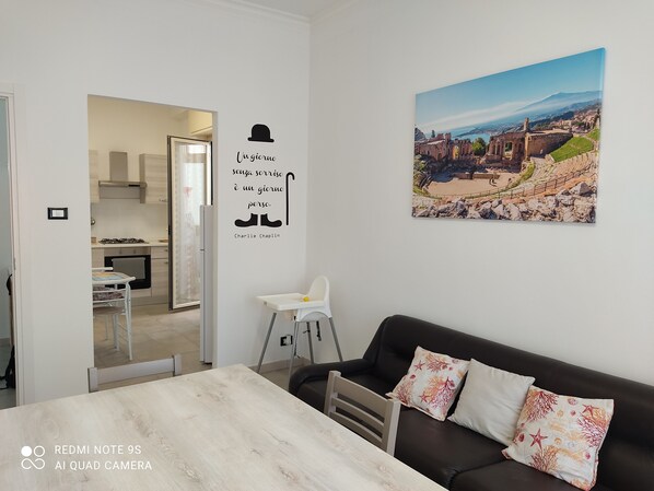 A modern living room with a dining area, a kitchen visible through an open door, and a scenic wall mural.