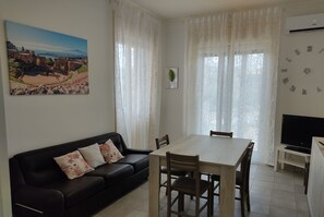A living room with a black sofa, a wooden dining table, and a TV.
