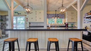 A kitchen with a central island, wooden stools, and pendant lighting. - Peaceful Lake House - Brand New Remodel (Macy)