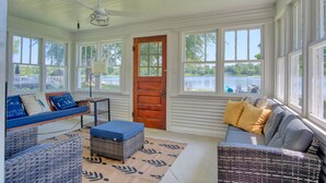 A sunroom with large windows, a wooden door, wicker furniture, and a view of a lake. - Peaceful Lake House - Brand New Remodel (Macy)
