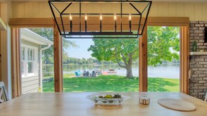 A dining area with a large table, a bowl of fruit, and a view of a lake and outdoor seating. - Peaceful Lake House - Brand New Remodel (Macy)