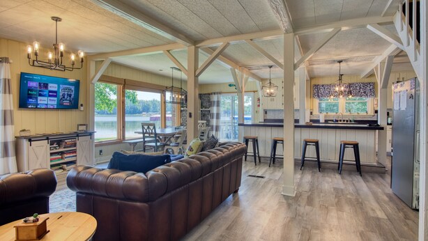 A spacious living room with a leather sofa, a wooden coffee table, and a TV mounted on the wall. - Peaceful Lake House - Brand New Remodel (Macy)