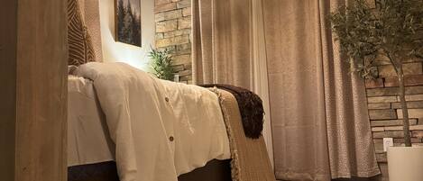 A bedroom with a bed, a ceiling fan, a stone wall, and a window with curtains.