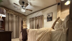 Un dormitorio con piso de madera, cama con ropa blanca, ventilador de techo y lámpara.