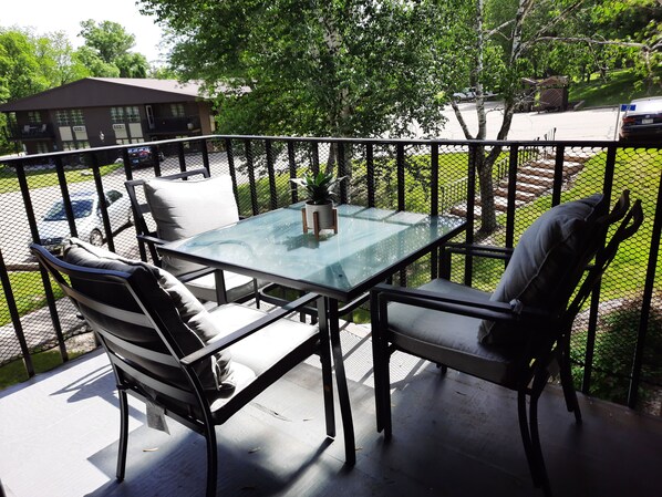 Relax on the patio with a glass-top table and two chairs, surrounded by lush greenery and a view of the surrounding area.