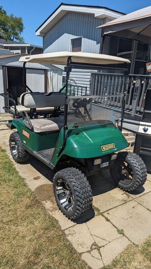 Ein grüner Golfwagen steht auf einer Betonfläche, im Hintergrund ist ein Haus zu sehen.