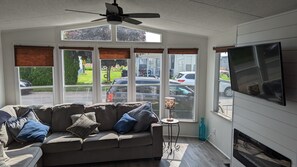 Ein Wohnzimmer mit einer Couch, einem Deckenventilator und großen Fenstern mit Jalousien.