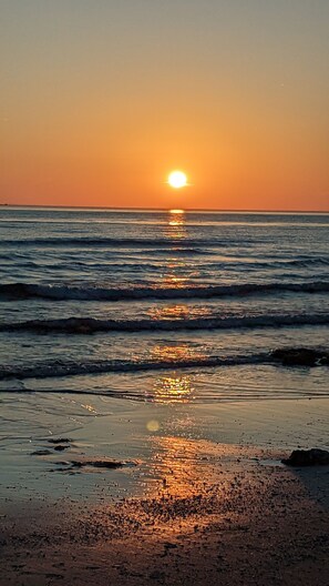 Una puesta de sol sobre el océano con olas que reflejan la luz del sol en la playa.