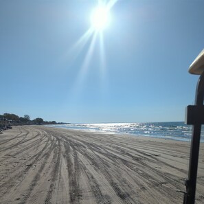 Ein Strand mit Radspuren, die zum Wasser führen, ein klarer Himmel und eine strahlende Sonne.