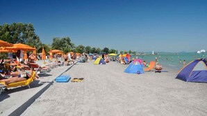 A beach with tents, umbrellas, and people sunbathing. - Holiday apartment Stylishly furnished with air conditioning (Balatonlelle)