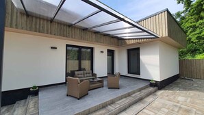 A modern patio with a glass enclosure, outdoor furniture, and a wooden deck. - Holiday apartment Stylishly furnished with air conditioning (Balatonlelle)