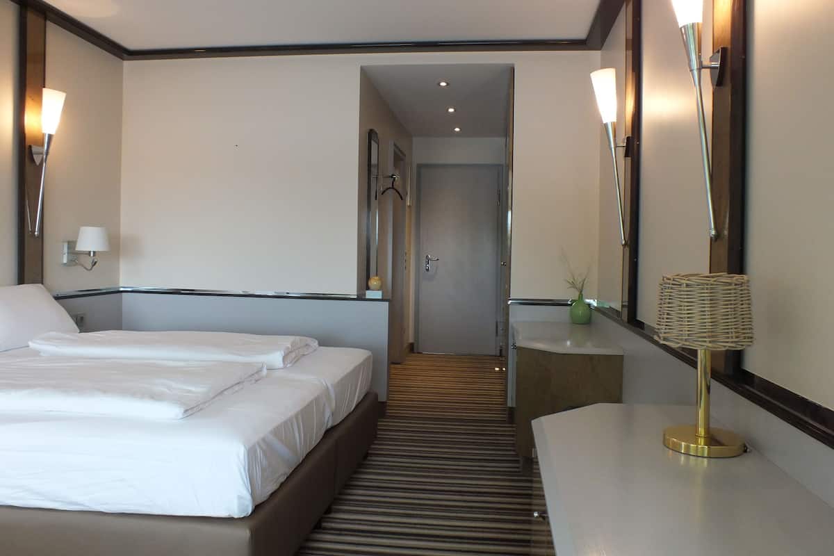 A hotel room with two beds, a desk, a mirror, and two wall-mounted lamps.