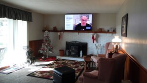 A living room with a fireplace, a Christmas tree, and a television displaying a news program. - 3 br country home close to town with hot tub (Muncie)