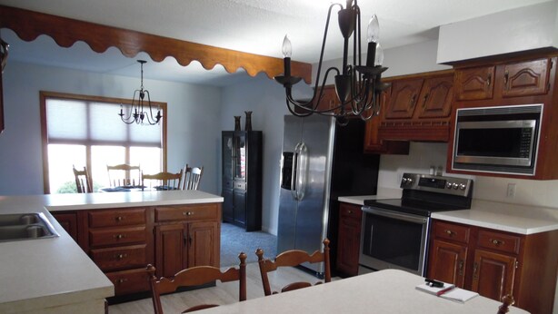 A kitchen with wooden cabinets, a stainless steel refrigerator, a microwave, and a dining area with a table and chairs. - 3 br country home close to town with hot tub (Muncie)