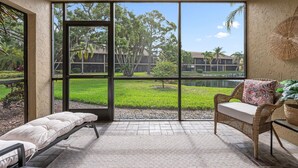 A room with a large window, a wicker chair with a cushion, and a bench. - Beautiful condo near Siesta Key and Siesta beach (Sarasota)