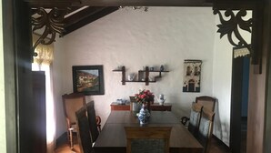 A dining area with a wooden table, chairs, a vase with flowers, and decorative shelves on the wall.