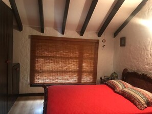 Ein Schlafzimmer mit einem hölzernen Bett, einer roten Bettdecke und einem Fenster mit Jalousien.