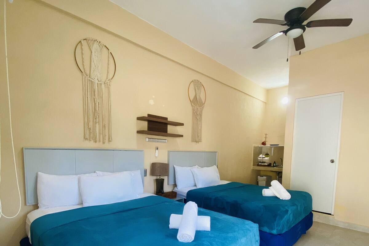 Habitación de hotel con dos camas, un ventilador de techo y decoración en la pared.