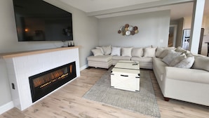 A modern living room with a fireplace, a sectional sofa, a coffee table, and a flat-screen TV mounted on the wall. - Luxury hillside house with a picturesque mountain view (Thornton)