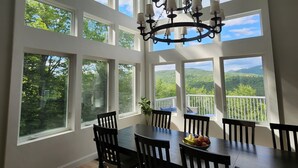 A dining room with a large table and chairs, surrounded by large windows offering a view of the outdoors. - Luxury hillside house with a picturesque mountain view (Thornton)