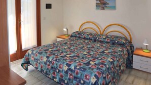 A bedroom with a floral bedspread, a wooden headboard, two bedside tables with lamps, and a wall sign with destination names.