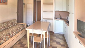 A compact living space with a sofa, dining table, chairs, a kitchen area with cabinets and a microwave, and a television.
