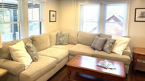 A living room with a beige sectional sofa, two wooden coffee tables, and a window with blinds. - Quarry Landing - Center of Town & River View - 3 Bedroom (Port Deposit)