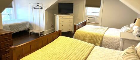 A bedroom with two beds, a dresser, a TV, and a window with blinds.