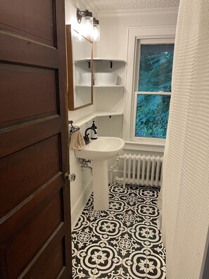 Une salle de bain avec un lavabo blanc, un miroir et une fenêtre donnant sur un paysage verdoyant.