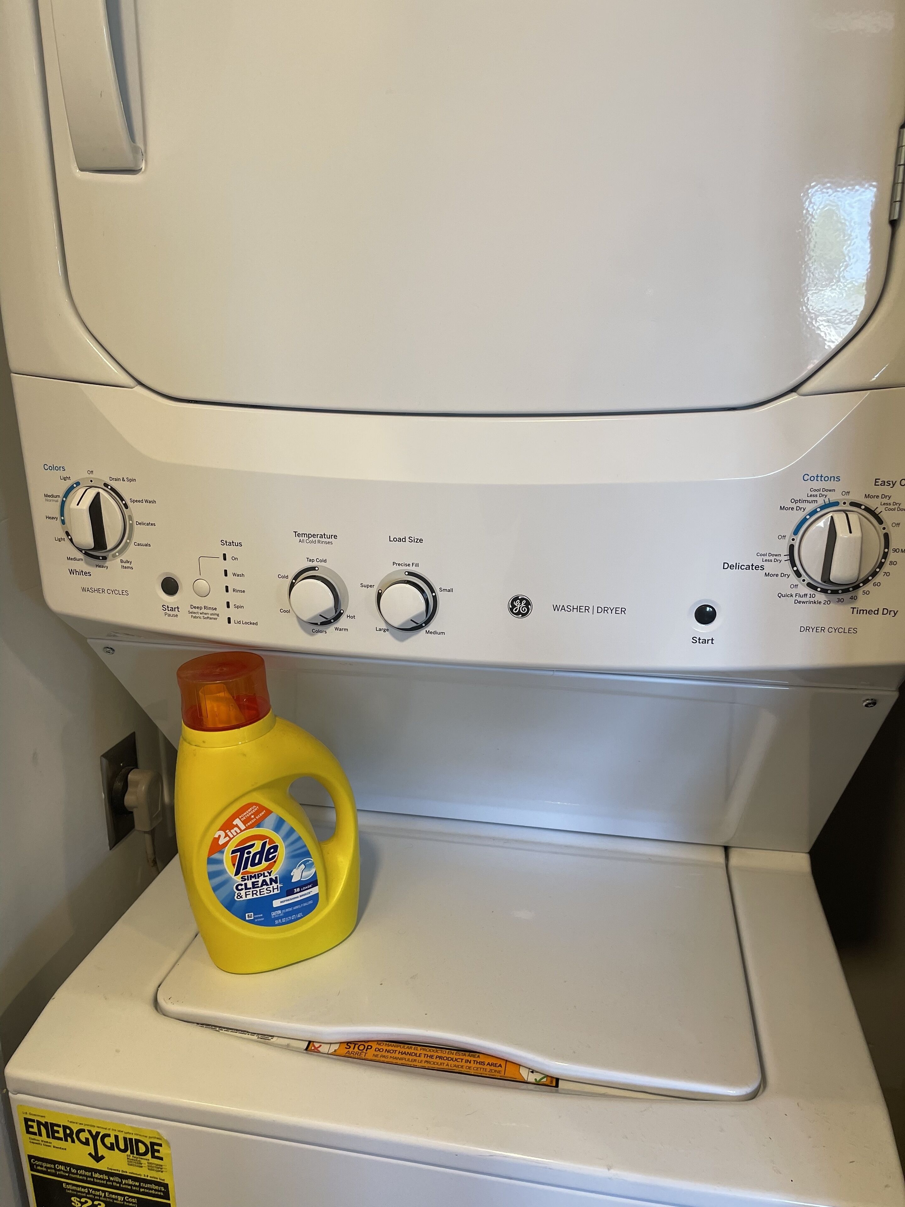 Een wasmachine met voorlader en een gele Tide wasmiddelfles erop.