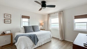Een slaapkamer met een bed, een plafondventilator, een nachtkastje, een lamp en uitzicht op het landschap door de ramen.