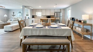 Een eetgedeelte met een tafel voor vier personen, houten stoelen, een witte tafelkleed en een rieten mand als decoratie.
