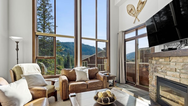 A spacious living room with a large window offering a mountain view, a fireplace, and a comfortable seating area. - Spacious 3bdrm Family Retreat Ski in/out w/hot tub (Sun Peaks)