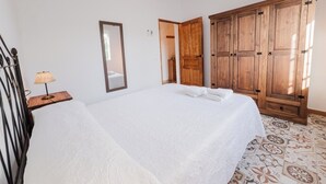 Un dormitori amb un llit, un armari de fusta, un mirall i una taula de nit amb una làmpada.