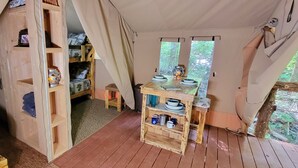 Een gezellige tent met een houten bed, een klein tafeltje met servies en planken met diverse spullen.
