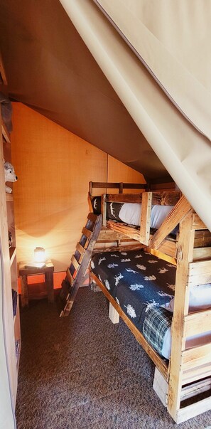 Une petite chambre mansardée, chaleureuse et accueillante, avec un lit superposé, un bureau doté d’une lampe et une échelle.