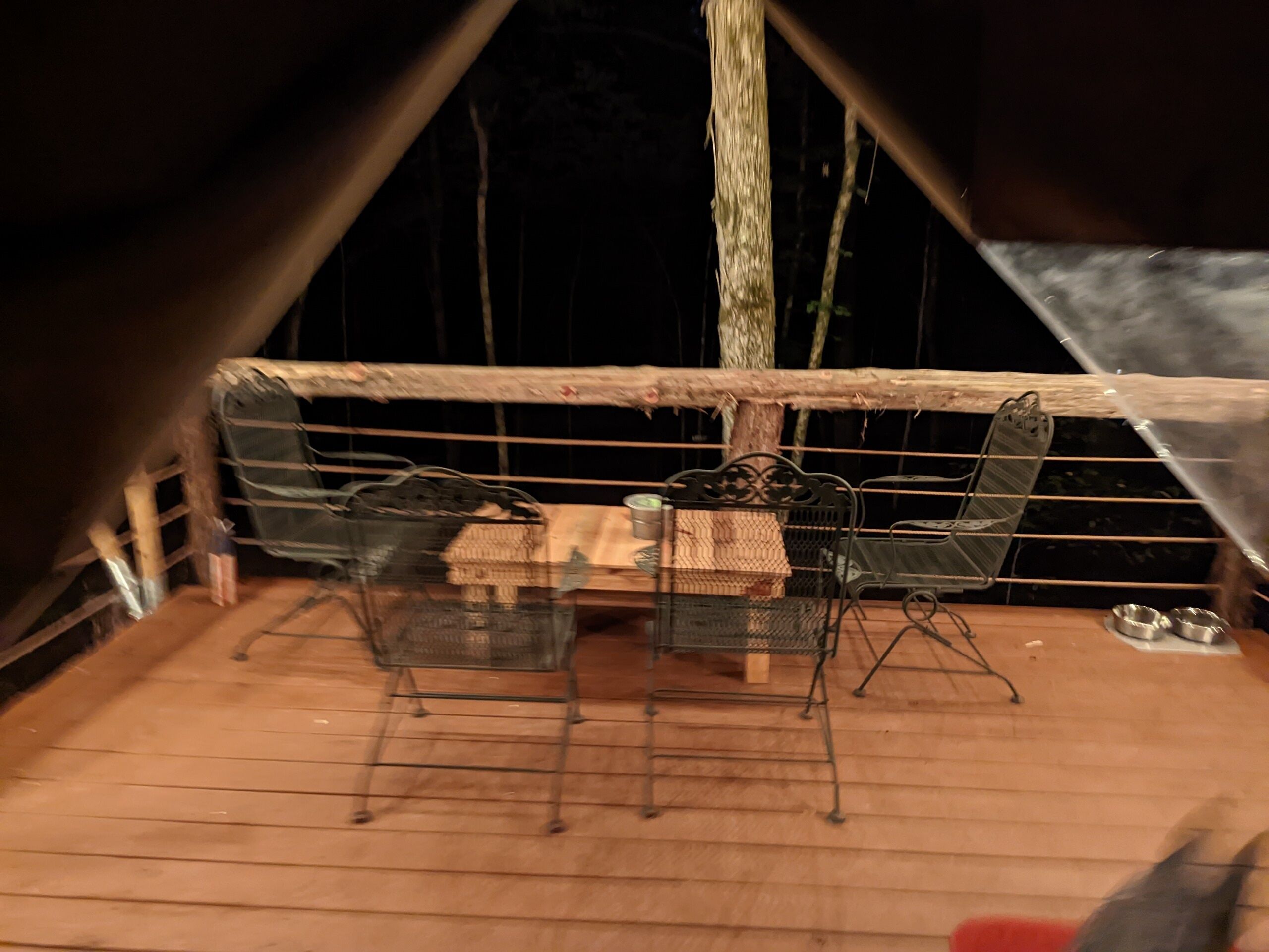 Een houten terras met een metalen tafel en stoelen, een klein tafeltje met een mand, en een metalen stoel met een mand.