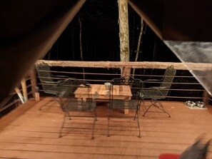 Une terrasse en bois avec une table et des chaises en métal, une petite table avec un panier, et une chaise en métal avec un panier.