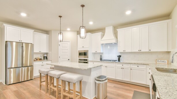 Una cocina moderna con armarios blancos, electrodomésticos de acero inoxidable, encimera de granito y una zona con taburete de bar.