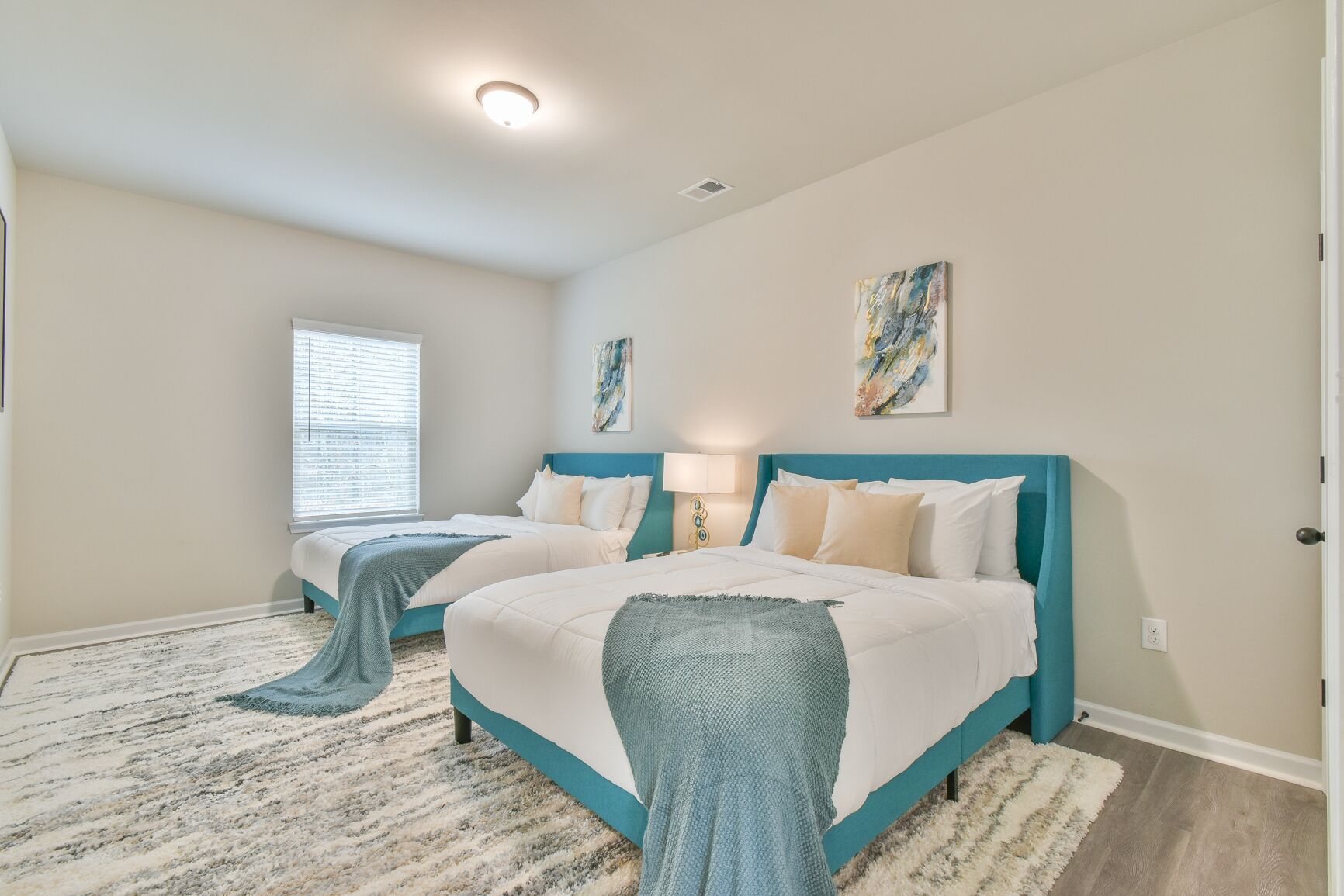A bedroom with two beds, a window, and artwork on the walls.
