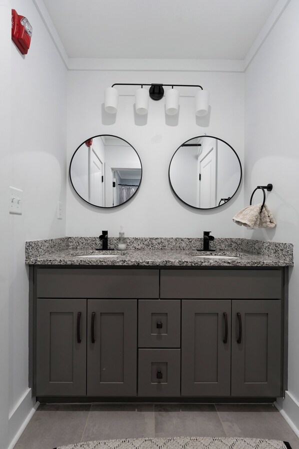A bathroom with two round mirrors, a granite countertop, and a towel rack. - The Manhattan Loft 4 (Cartersville)