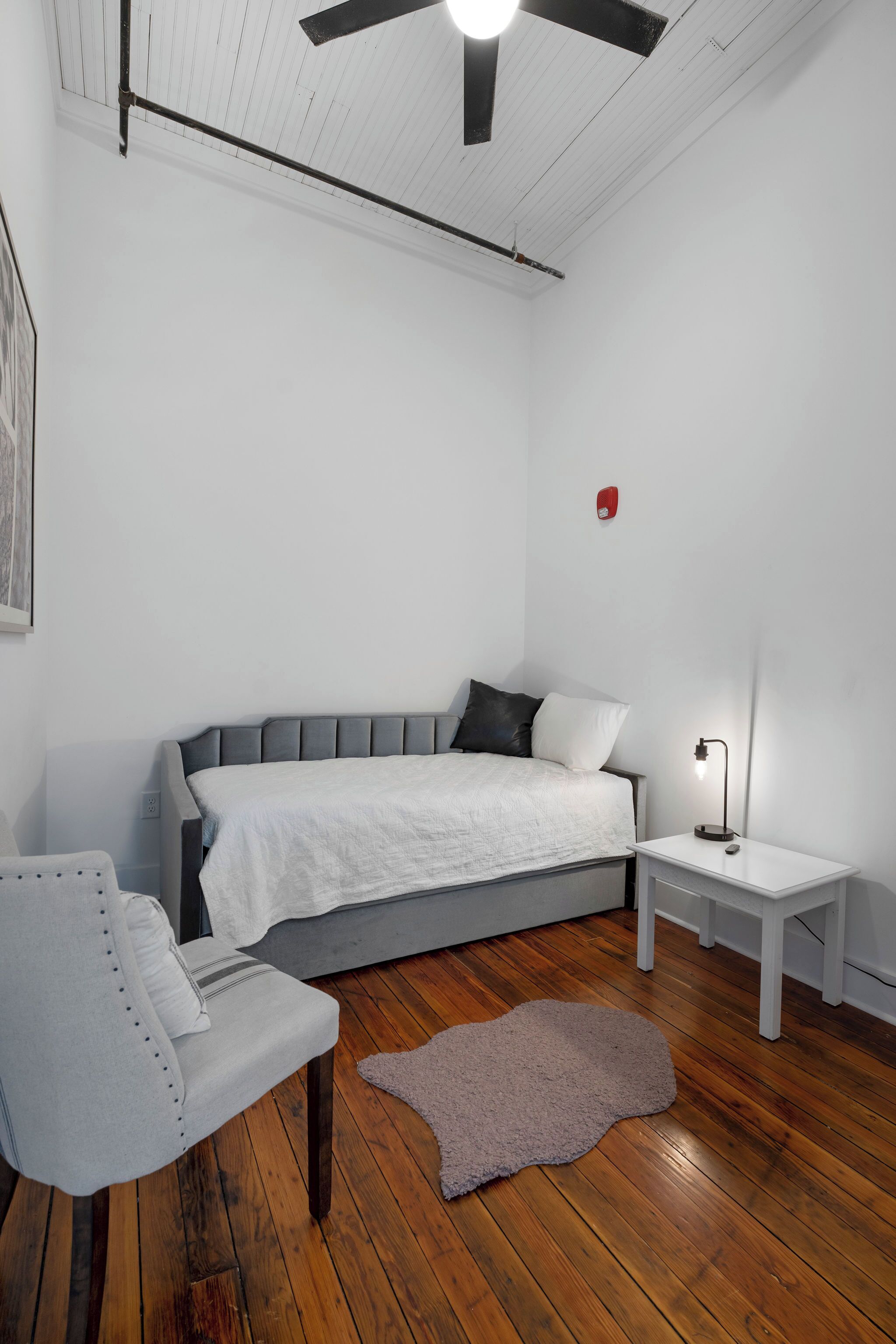 Un dormitorio con cama, mesita de noche, silla y ventilador de techo.