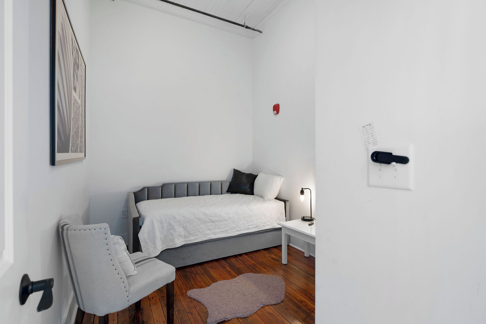Ein modernes Schlafzimmer mit Bett, Nachttisch, Sessel und einem kleinen Teppich.