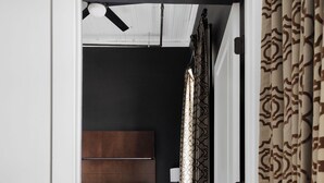 A hallway leading to a bedroom with a wooden floor, a bed with white bedding, and a dark-colored headboard. - Soho Loft 5 (Cartersville)